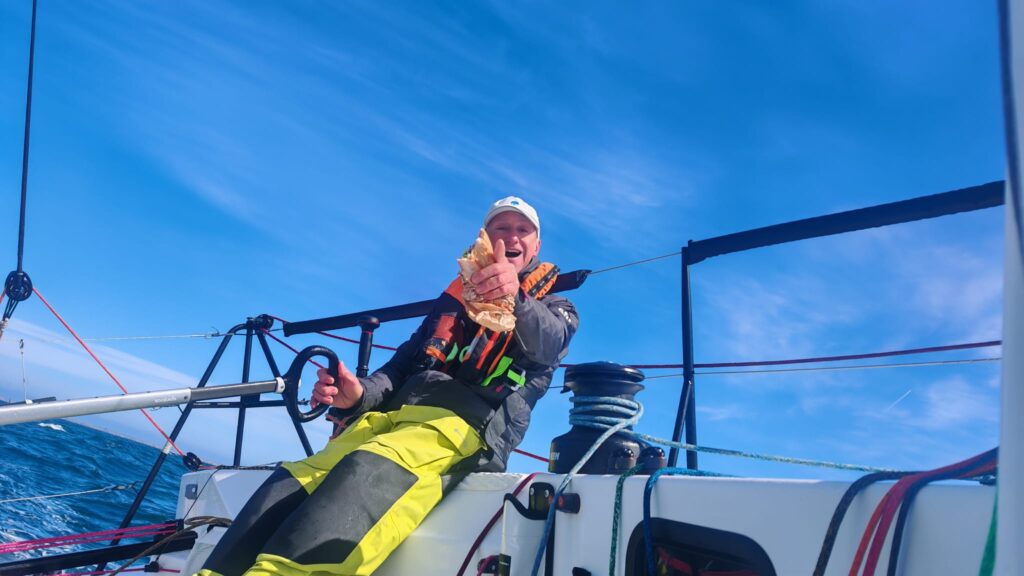 JP Kelbert à la barre du JPK 1050 PERSAIVERT en train de manger un sandwich